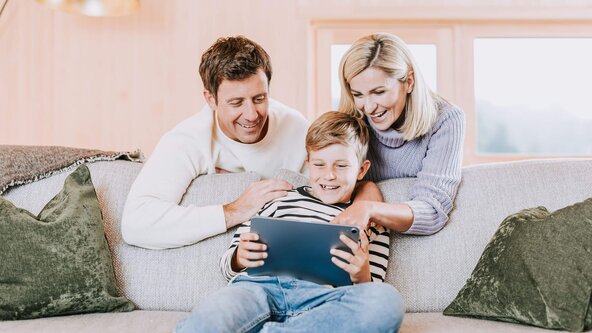 Familie sitzt in Wohnzimmer auf Sofa und spielt mit Tablet