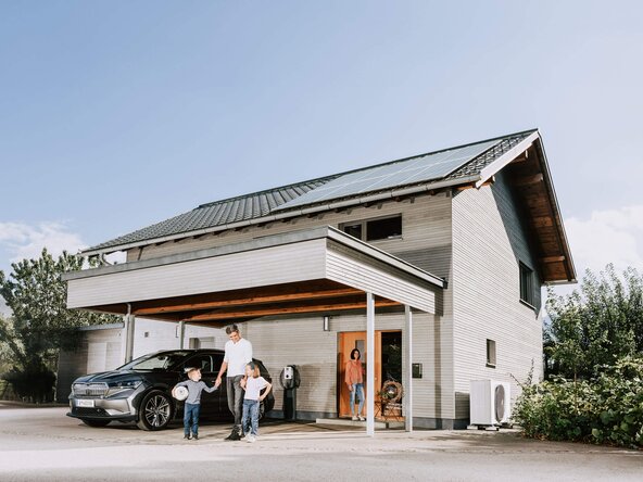 Familie steht vor Einfamilienhaus mit Photovoltaikanlage, Wärmepumpe und Wallbox