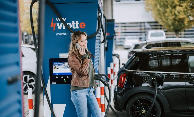 Junge Frau telefoniert, während ihr Fahrzeug am Schnelllader auflädt