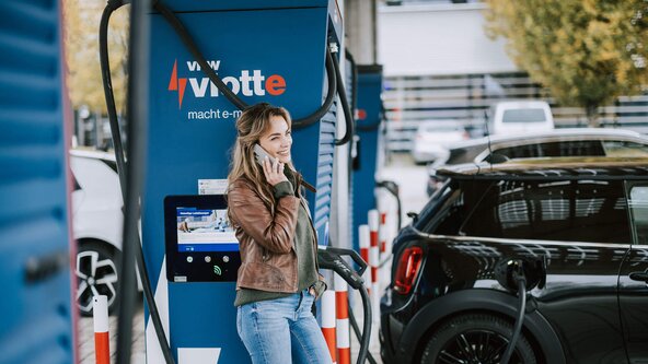 Junge Frau telefoniert, während ihr Fahrzeug am Schnelllader auflädt