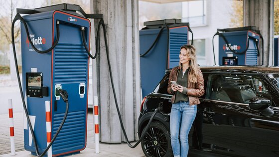 Frau lehnt sich an ihrem Auto an. während das Fahrzeug am Schnelllader auflädt