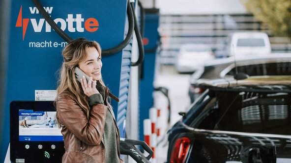 Junge Frau telefoniert, während ihr Fahrzeug am Schnelllader auflädt
