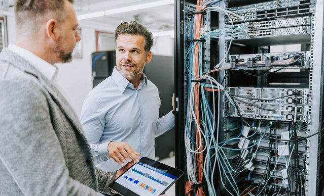 Zwei Männer diskutieren mit einem Tablet in der Hand vor einem Serverschrank