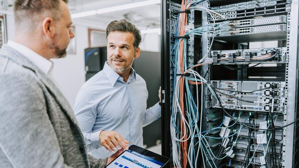 Zwei Männer diskutieren mit einem Tablet in der Hand vor einem Serverschrank