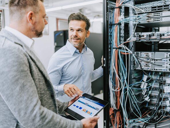 Zwei Männer diskutieren mit einem Tablet in der Hand vor einem Serverschrank