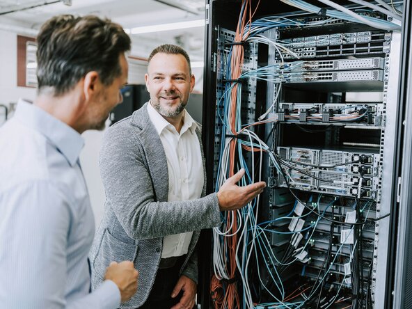 Zwei Männer diskutieren mit einem Tablet in der Hand vor einem Serverschrank
