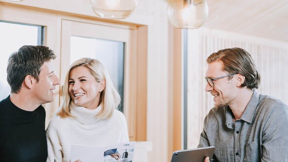 Energieberater sitzt bei Familie am Tisch und zeigt etwas auf dem Tablet
