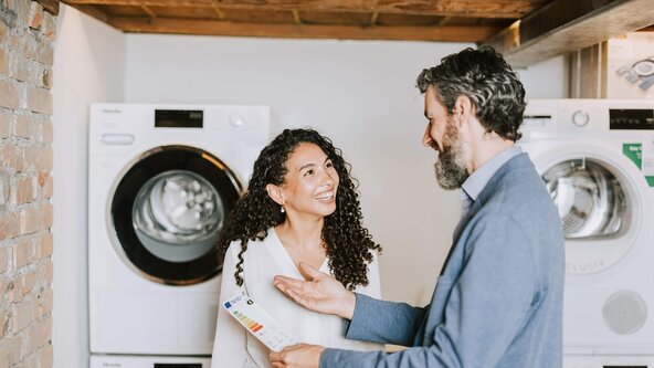 Mann erklärt Frau Energiesparlabel an einer Waschmaschine