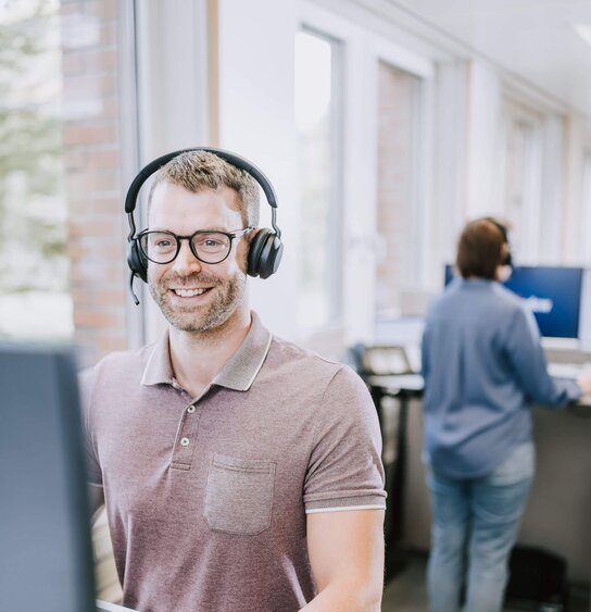 Kundenservicemitarbeiter sitzt mit Headset vor dem Bildschirm
