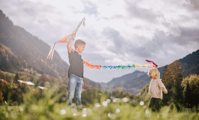 Zwei Kinder spielen mit einem Drachen auf der Wiese
