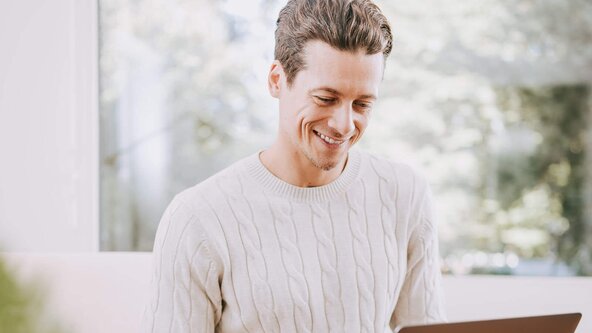Mann mit Laptop sitzt auf Couch