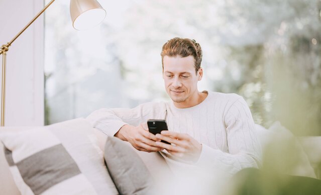 Mann mit Smartphone sitzt auf Couch