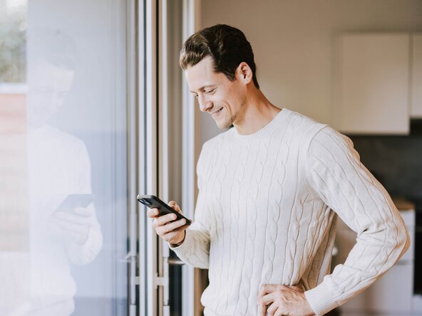 Mann mit Smartphone steht vor Fenster