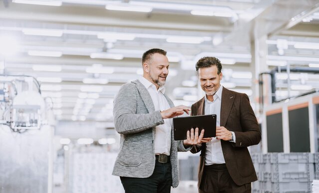 Kundenbetreuer führt Gespräch mit Unternehmer in Produktionshalle