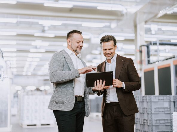 Kundenbetreuer führt Gespräch mit Unternehmer in Produktionshalle
