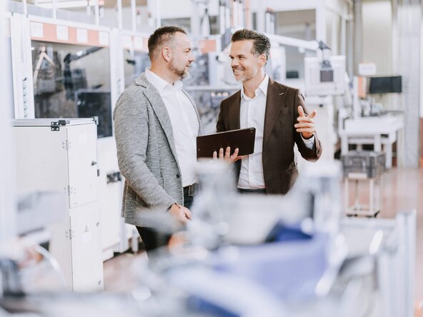 Kundenbetreuer führt Gespräch mit Unternehmer in Produktionshalle