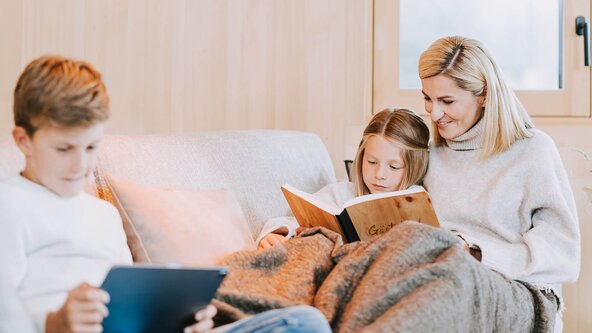 Familie sitzt gemütlich auf der Couch und liest ein Buch