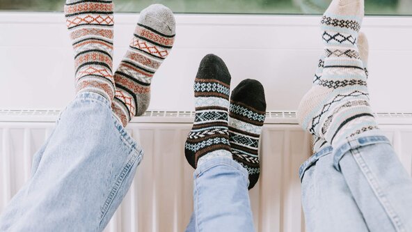 Drei paar Füße mit Wollsocken auf einem Heizkörper