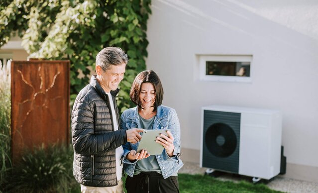 Ein Mann und eine Frau stehen mit einem Tablet vor einer Luftwärmepumpe